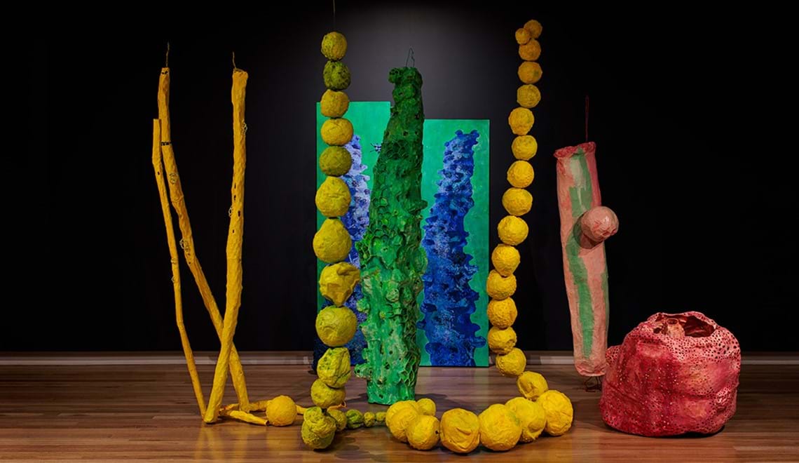 A colourful artwork by Chris DeRosa with brightly coloured papier mache shapes. It is titled Under here my dreams are made of water.