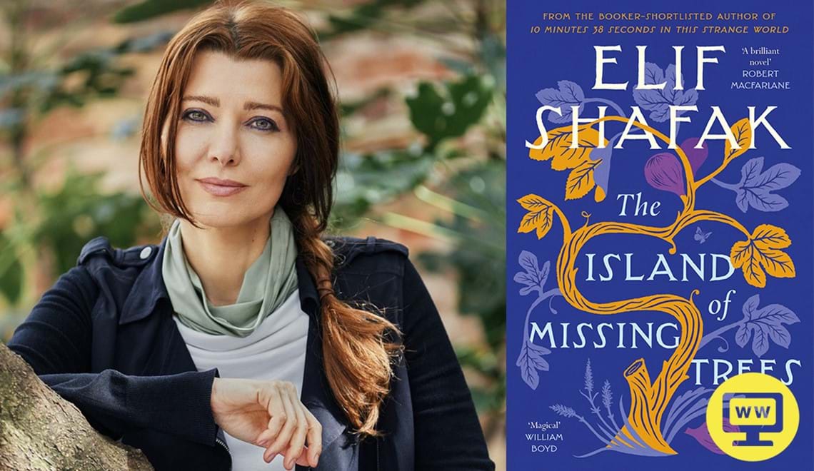 Elif Shafak has long brown hair that is pulled to the side, she wears a blue jacket over a grey shirt and leans on a tree