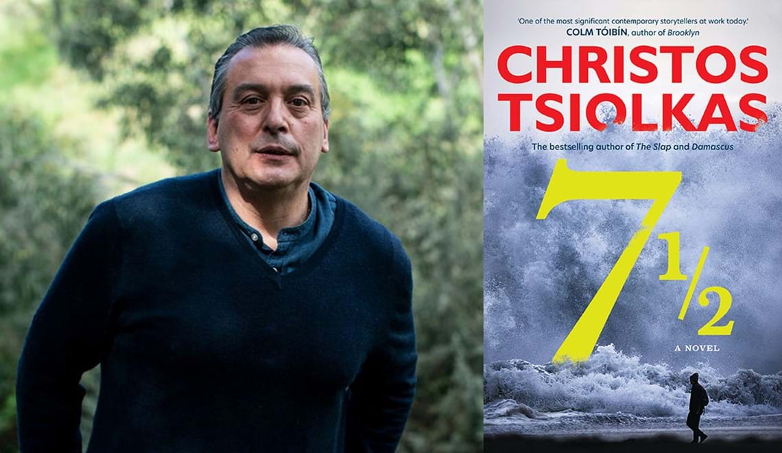Christos Tsiolkas stands outdoors, he wears a blue knitted jumper over a blue shirt, he has short hair and is smiling