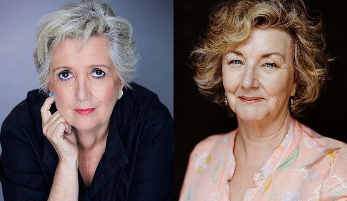 Jane Caro has short grey hair and is wearing a black shirt and pink lipstick. Debra Oswald is wearing a light pink blouse and has short blonde hair. Both writers are smiling at the camera.