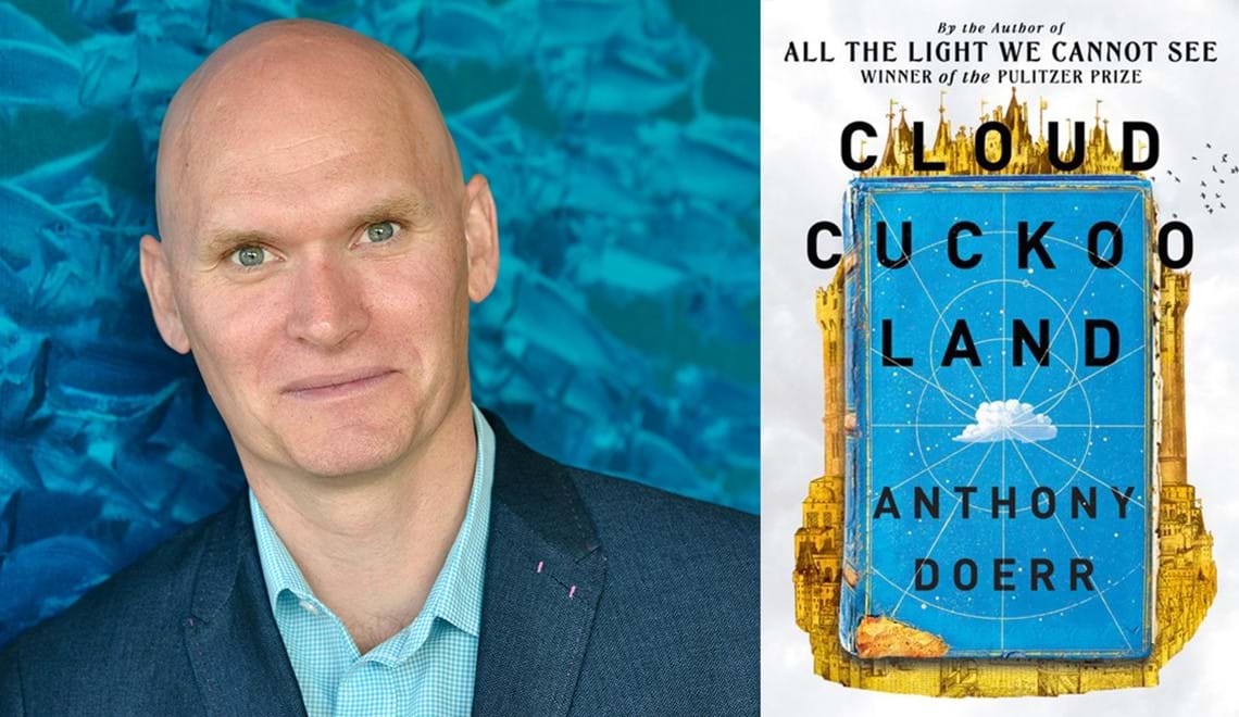 Anthony Doerr is bald and has blue eyes. He is wearing a lightl blue shirt with a dark blue jacket and standing in front of an aqua background. He is slightly smiling at the camera and seems almost as though he is suppressing a laugh.
