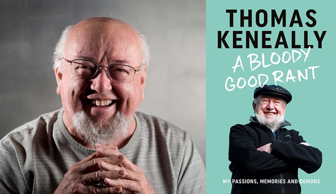 Thomas Keneally has white hair, a white beard and wears a grey t-shirt. He's smiling broadly at the camera with his hands clasped in front of him.