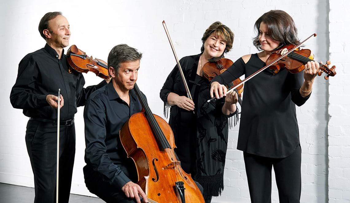 Four people, two men and two women, are wearing black and holding string instruments.